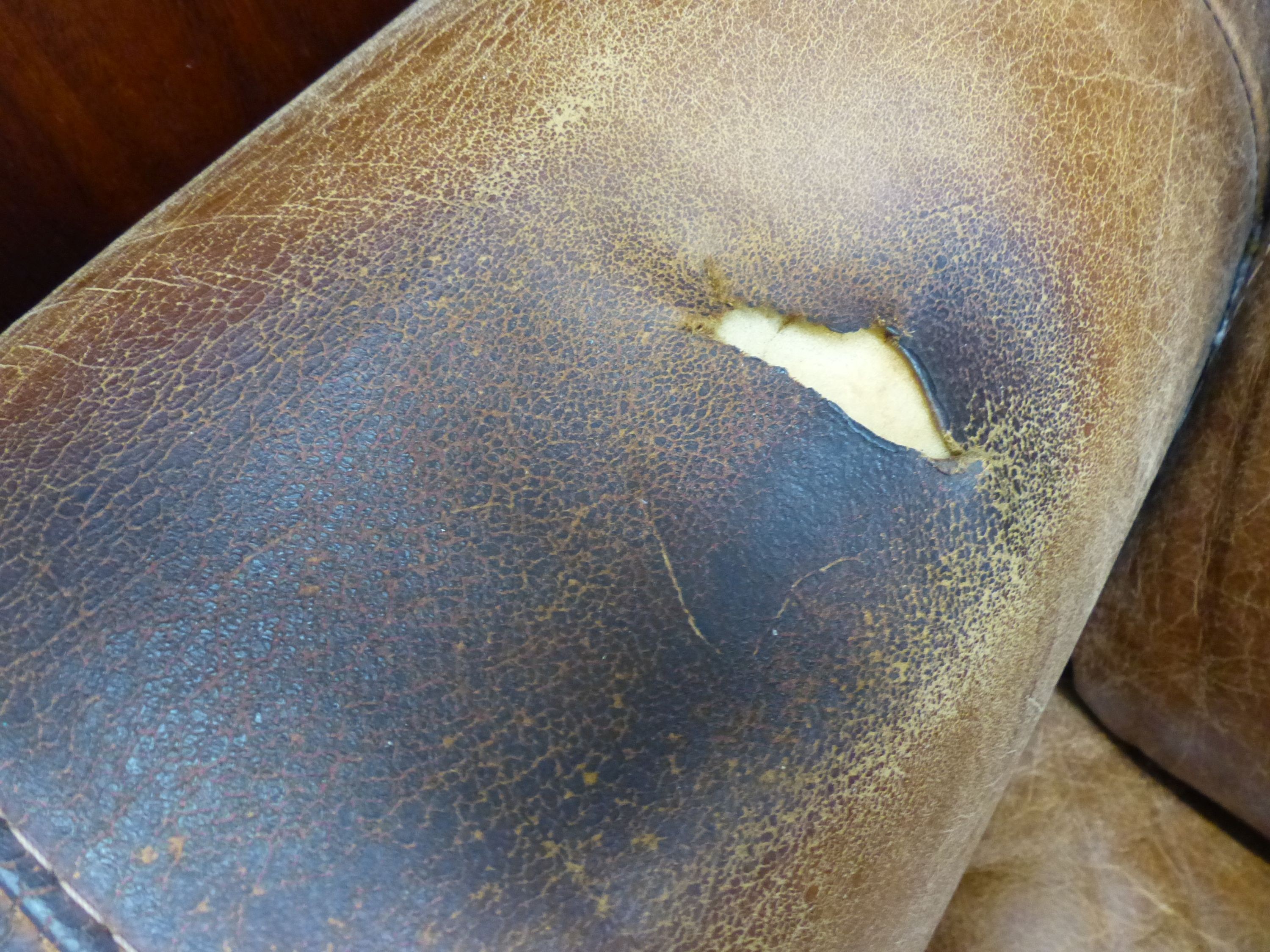 A pair of tan leather armchairs, W.94cm D.94cm H.90cm (one arm holed)